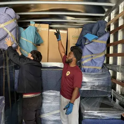Two movers in Elite Star shirts and gloves stacking padded furniture inside a moving truck