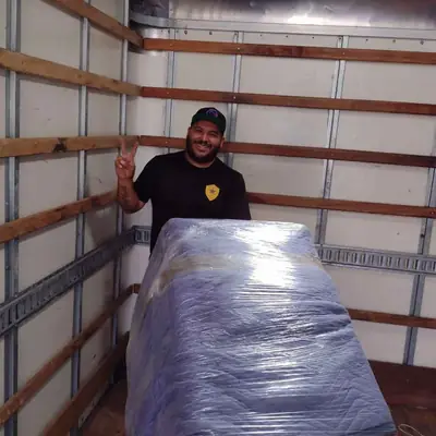 Mover standing beside a shrink-wrapped, blanket-padded piece of furniture inside the truck