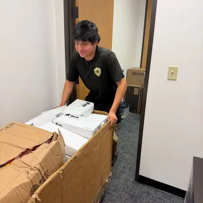 Mover rolling a cart of boxed office equipment down a hallway
